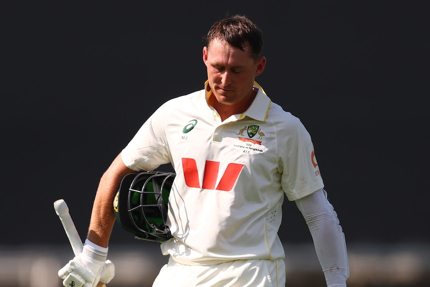 A cricketer with bat in hand trudges off the field while looking down