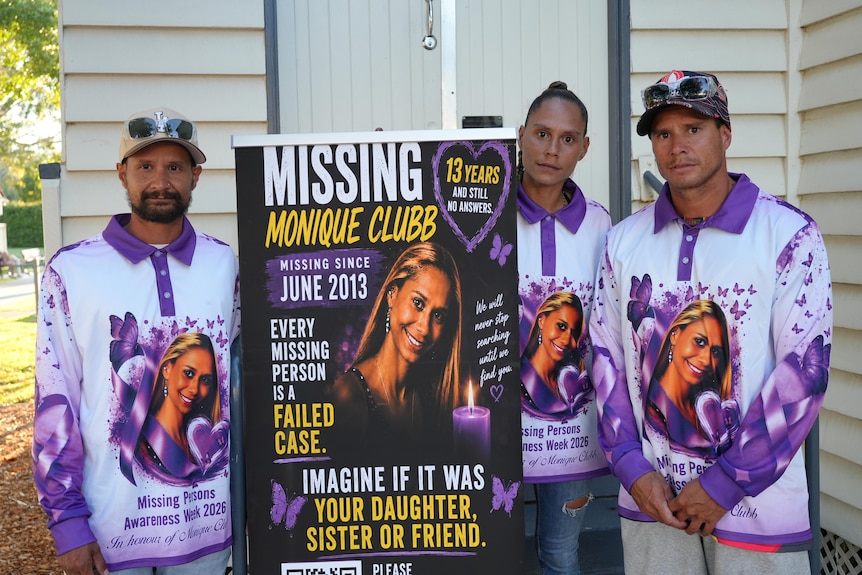 Three siblings wearing matching purple shirts hold up a large poster.