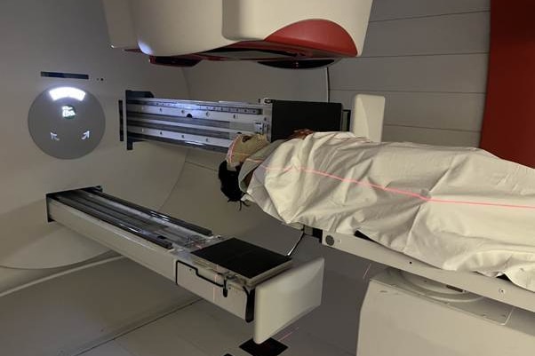 A person covered by a blanket as they lay in between two elongated machines with laser lines over their body
