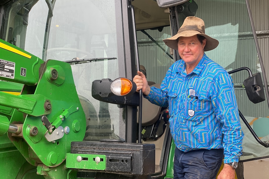 A man in a battered hat leaning next to a tractor
