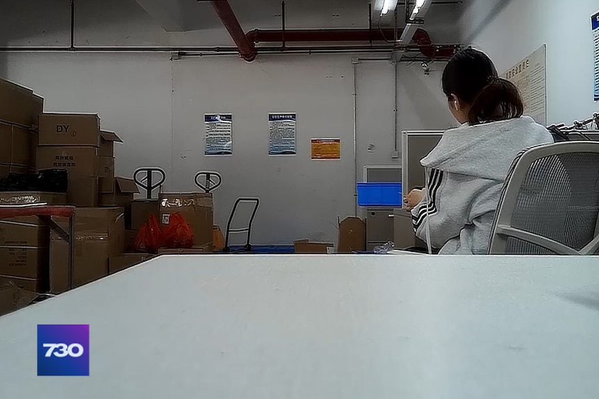 A woman can be seen sitting at a desk inside a factory.