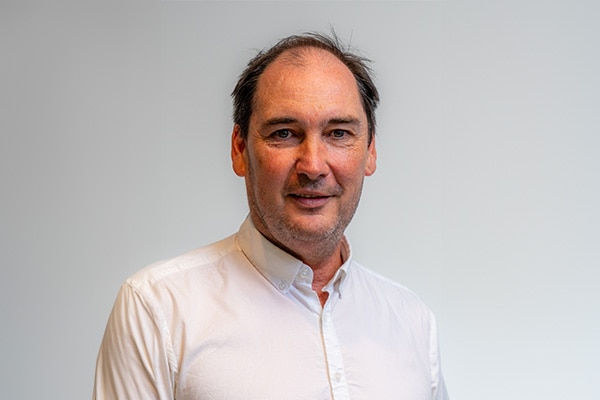 A dark-haired, middle-aged man in a business shirt poses for a corporate headshot.