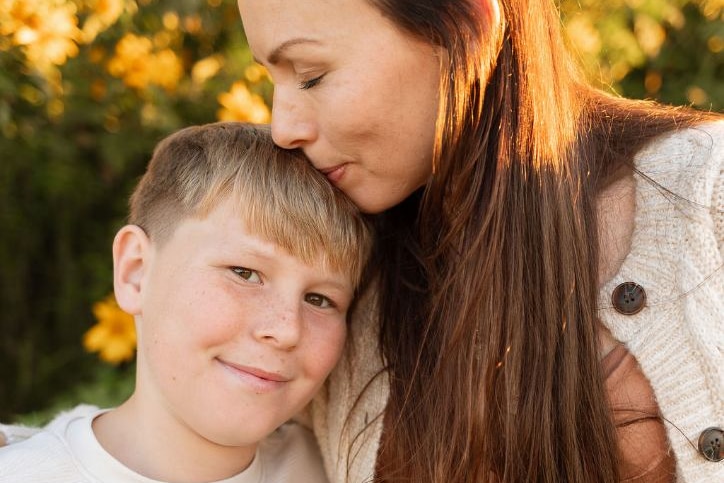 A woman with long hair kisses the top of a young boy's head.