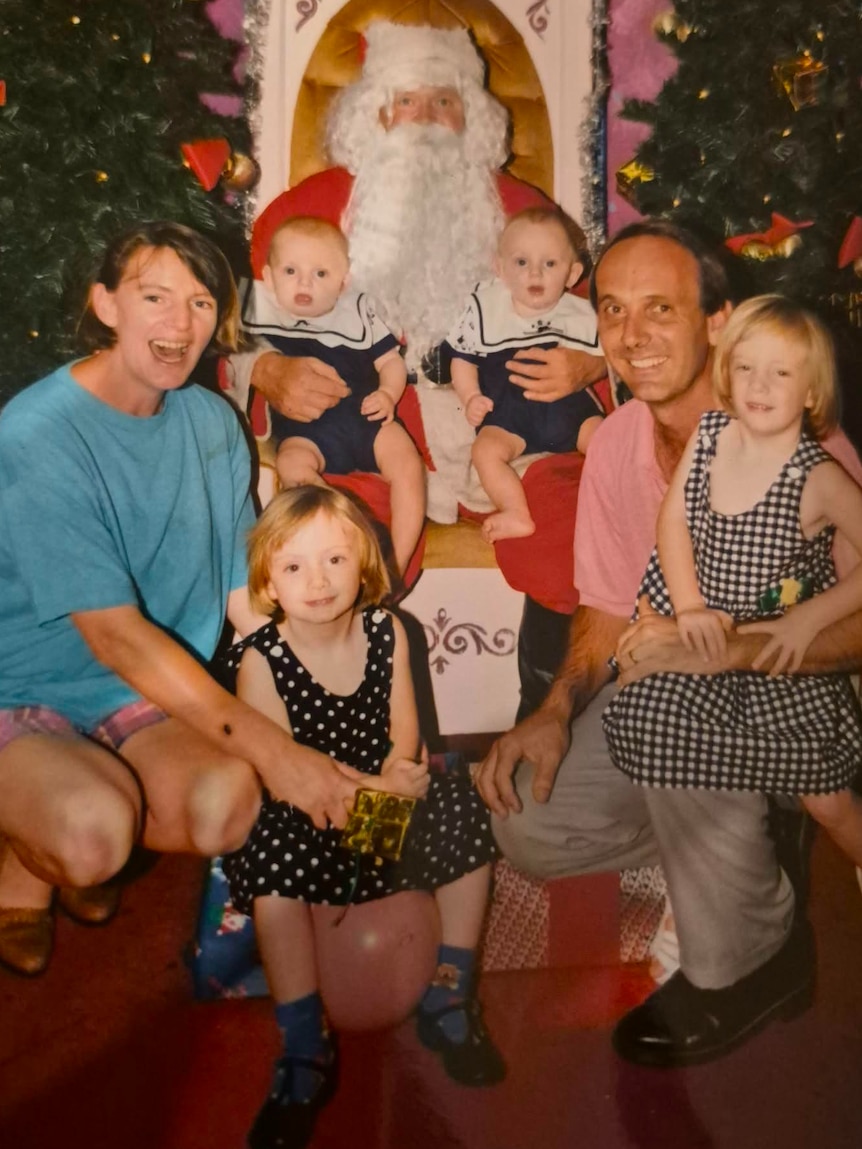A family with two babies, twin toddlers, mum and dad pose together with Santa