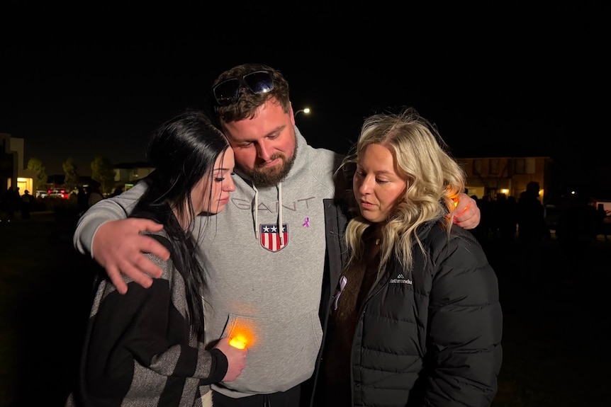 Three people share a hug in commiseration