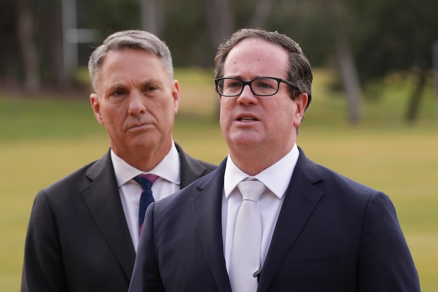 Two men in suits and ties stand on a green lawn.