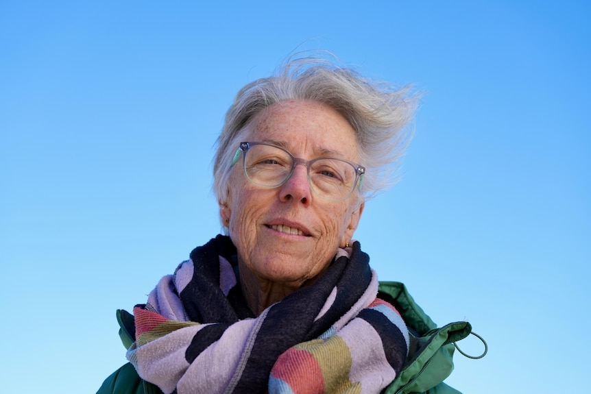 a low camera angle looking up at Susan Belperio at Glenelg Beach, wearing a warm scarf.