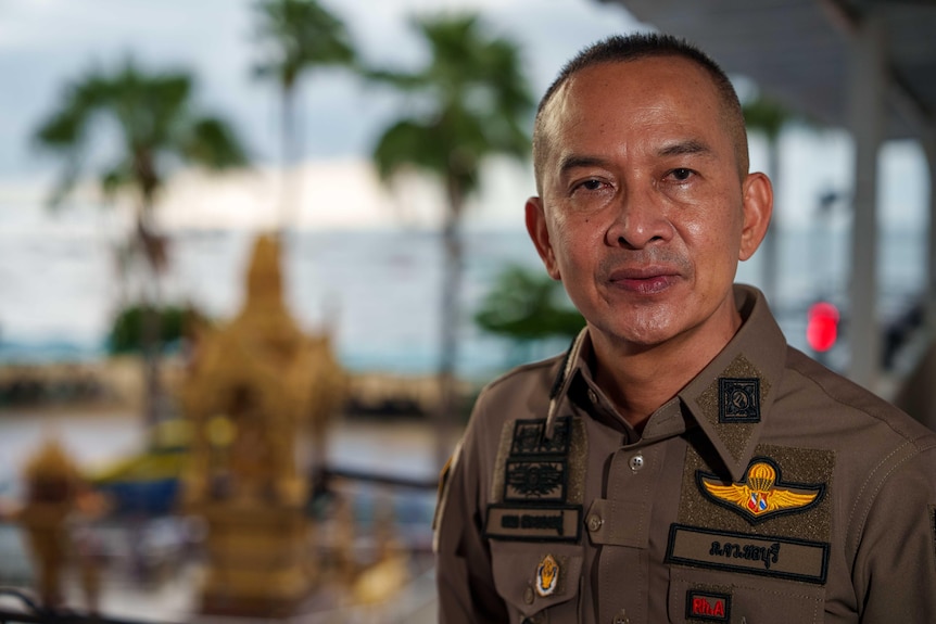 A man wearing a brown police uniform looks towards the camera.