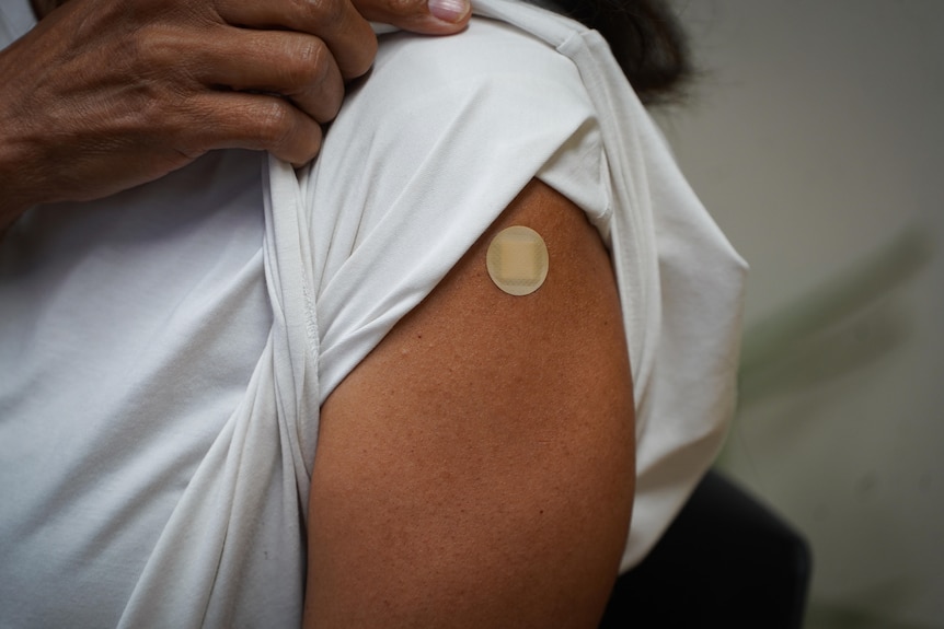 A woman holding up her t-shirt sleeve, revealing a small band-aid over the spot where she was vaccinated.