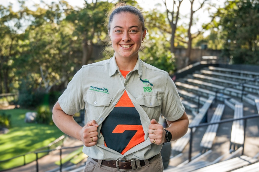 Woman with zoo keeping shirt which is slightly unbuttoned to reveal orange AFL jersey underneath like superman
