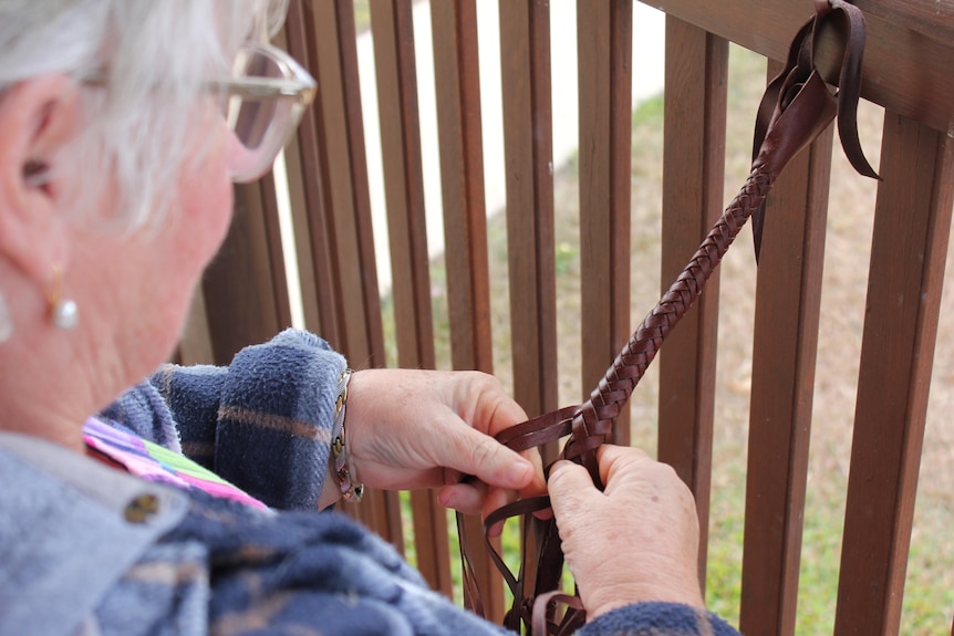 A woman's hands plait brown kangaroo leather into a rounded long tail.