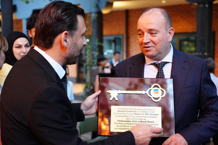 Mr Ahmed smiling with emotion as he holds a plaque with a gold key on it being presented to him by the mayor.