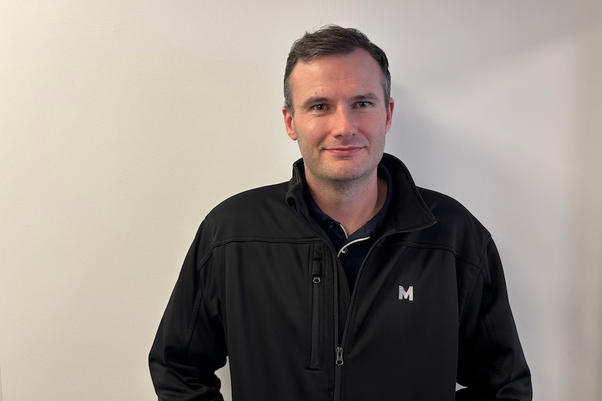 A smiling, dark-haired man in a black zip-up jacket.