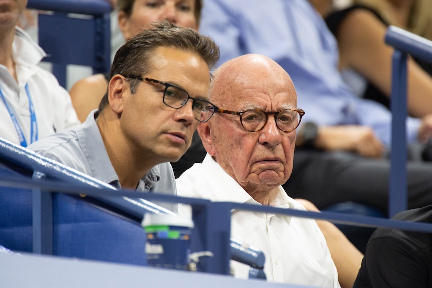 A young man and an older man sit together in sporting stands