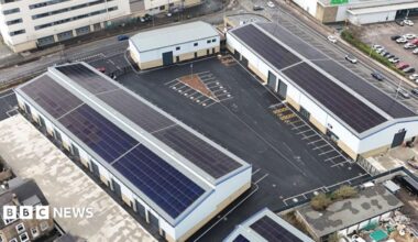 An aerial shot of a business park, with large white warehouse-style buildings surrounded by roads and car parks.