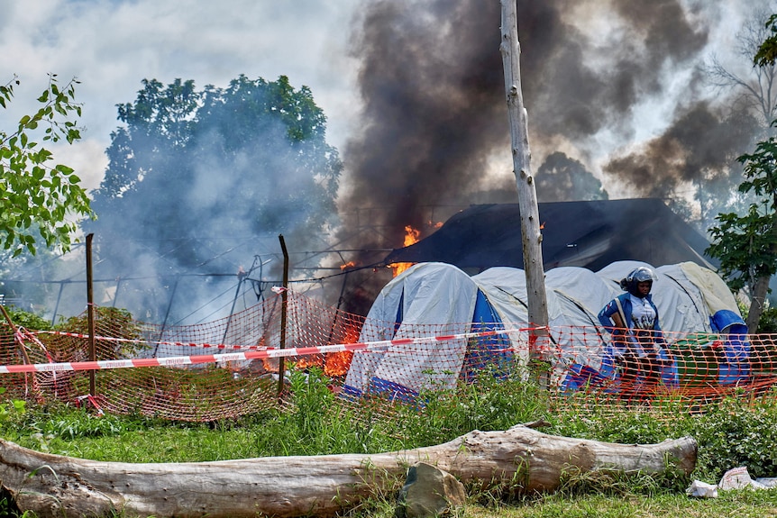 Medical tents burn behind a Congolese police officer in the middle of the day.