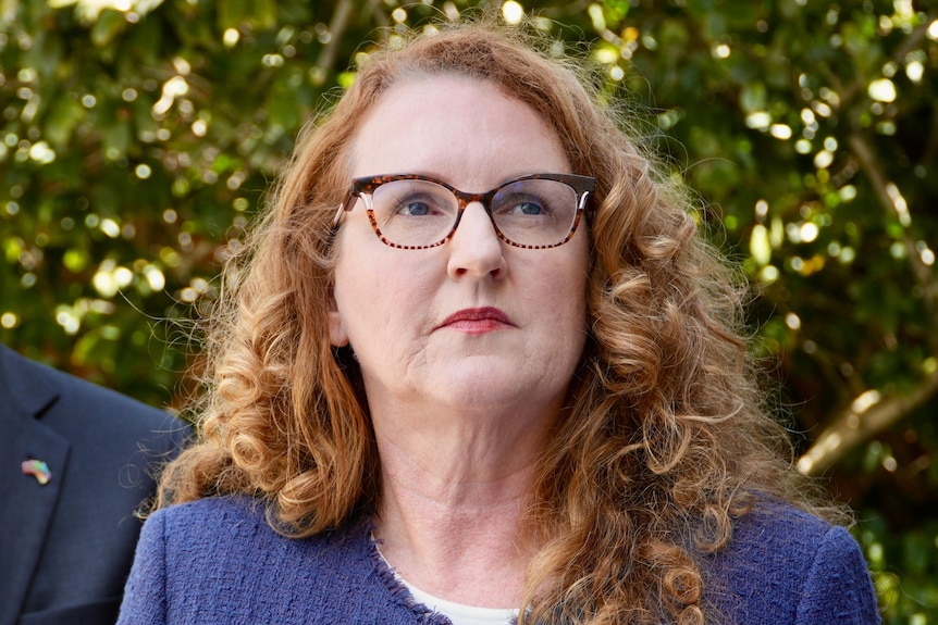 Katrina Stratton standing in front of microphones holding a book