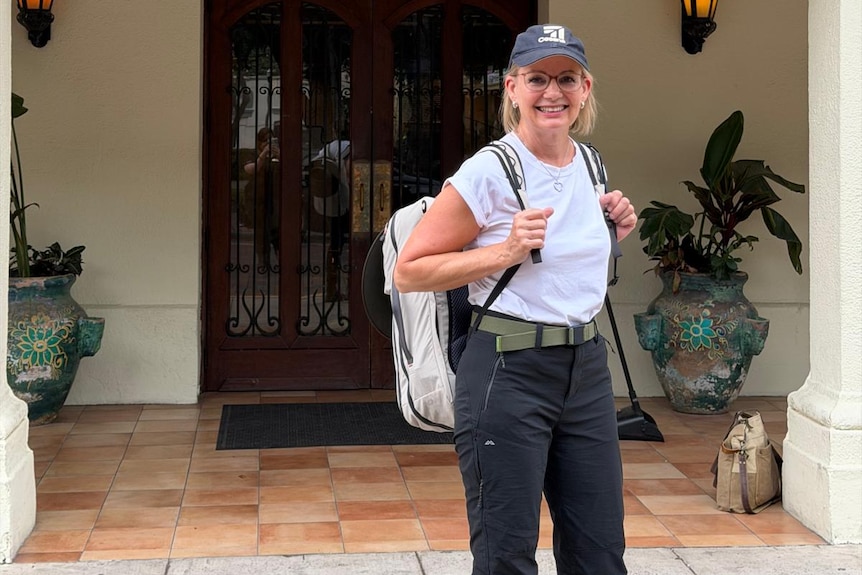 Sussan Ley in a white shirt and dark pants with a backpack outside a building.