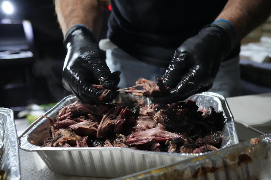 A tray of smoked, juicy meat being shredded by hand