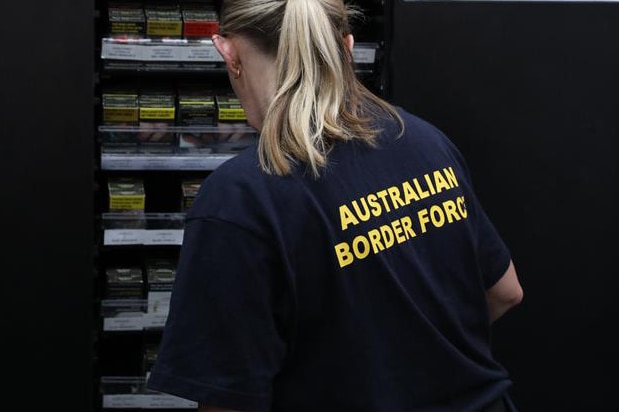 An Australian Border Force employee infront of cigarettes.