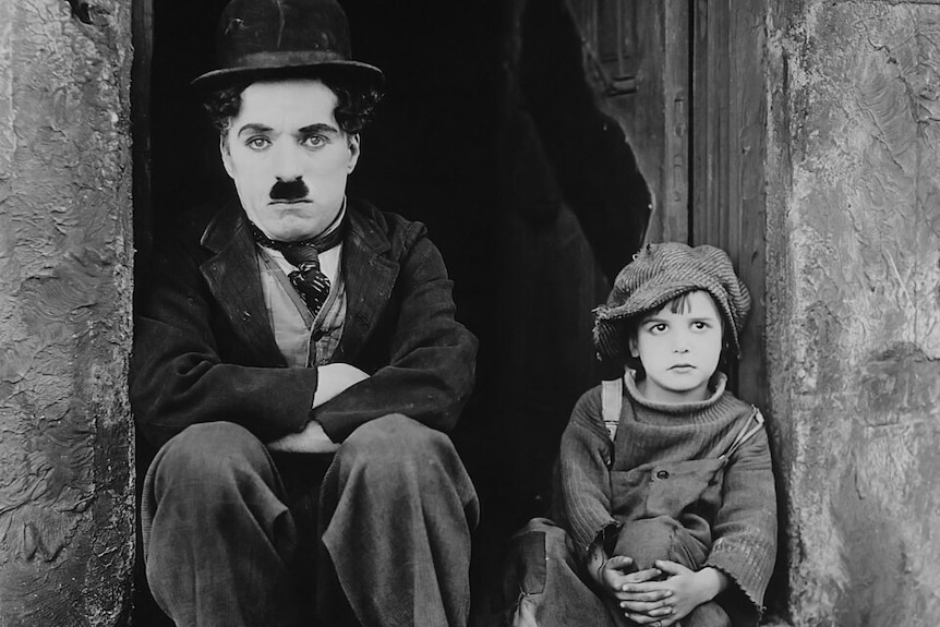 Charlie Chaplin sits on a footstep next to a young boy.