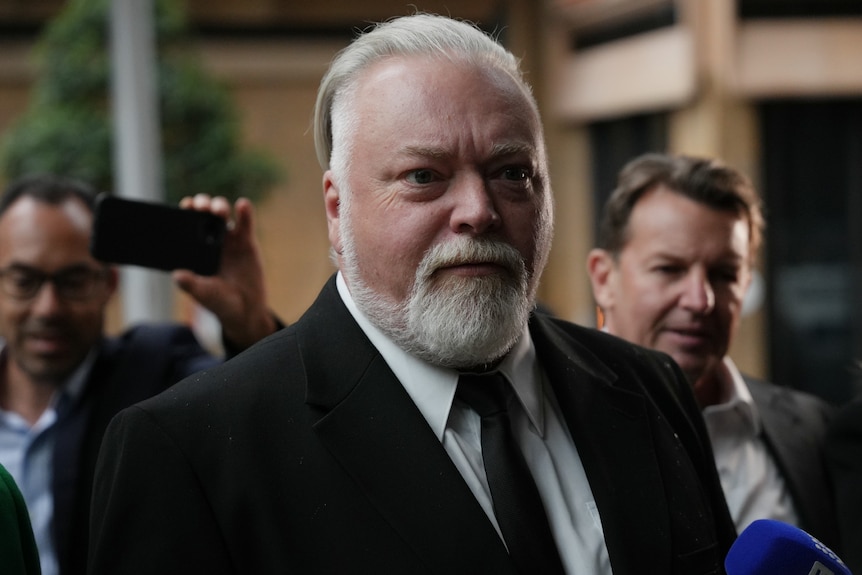 Mr Sandilands wearing a suit talking to reporters outside court.