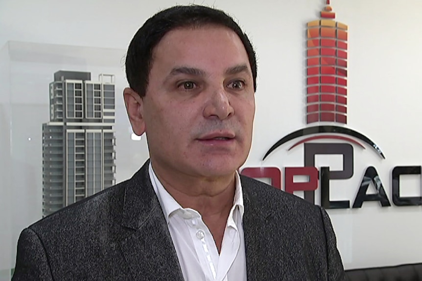 fugirive property developer jean nassif looks at the camera in a front of a signthat read toplace