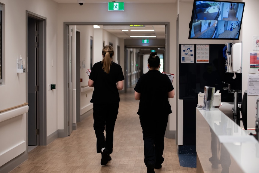 Two nurses walk down a hospital corridor seen from behind.