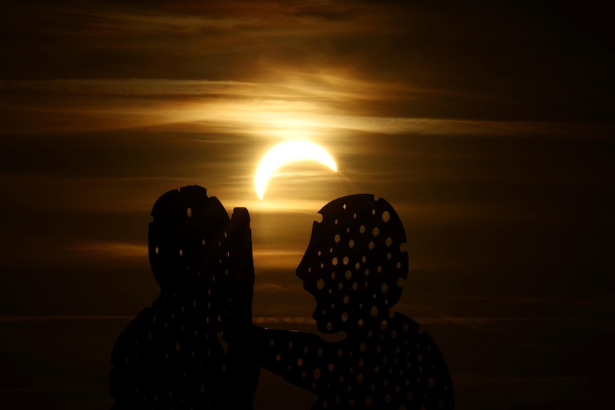 A partial eclipse shines through a statue with holes through it.