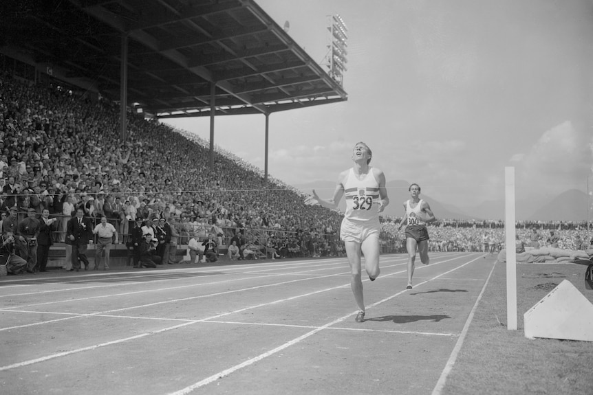 A black and white image of Roger Bannister crossing the line in a stadium after running the mile