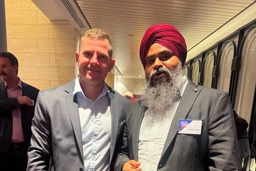 Luke Herdegen and Parminder Singh standing next to each other wearing grey blazers
