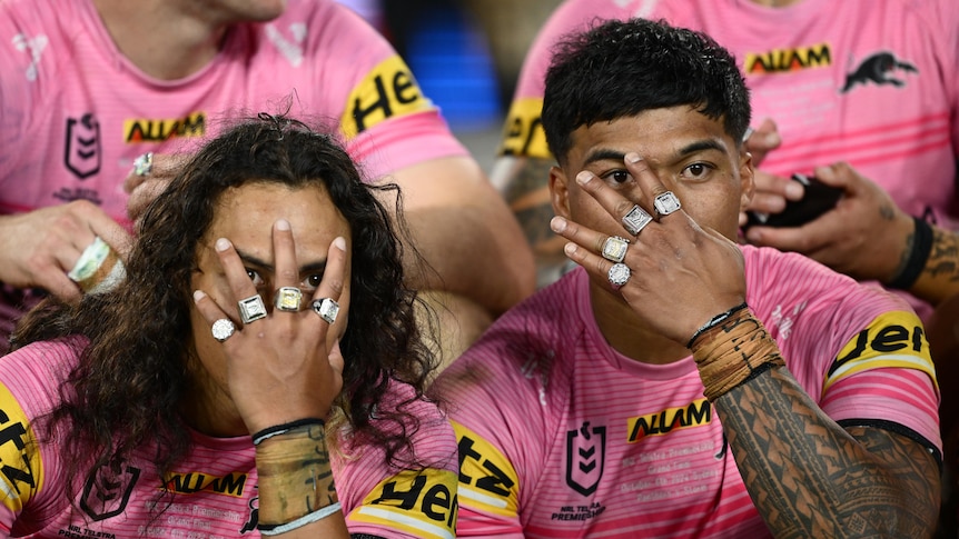 Two Penrith Panthers men's NRL players hold their hands in front of their faces, highlighting four premiership rings each.