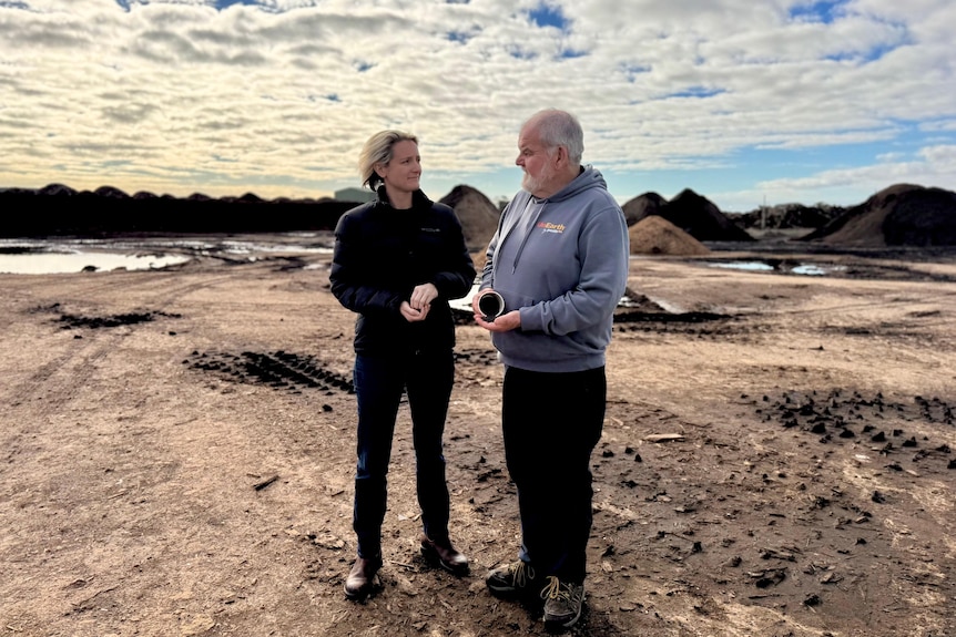 Two people talk to each other while standing on dirt and holding soil samples.