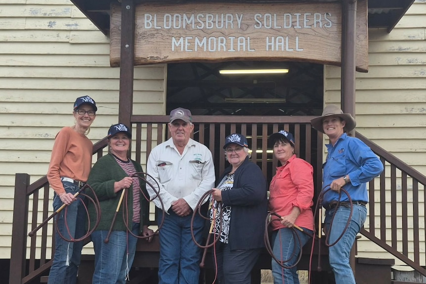 A group of five women and one man stand smiling at the camera whilst holding stock whips coiled up in their hands.
