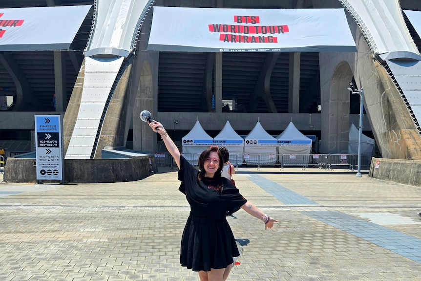A woman in black holding posing outside a concert hall.