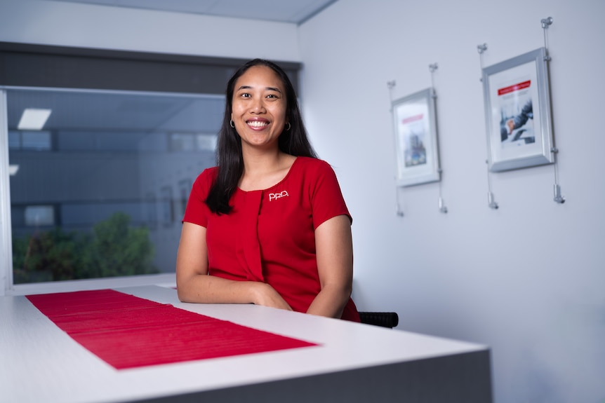 A woman in a red shirt next to a desk 