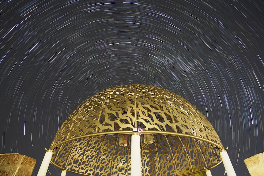 Blurred stars in a dark, clear sky above a golden dome structure.