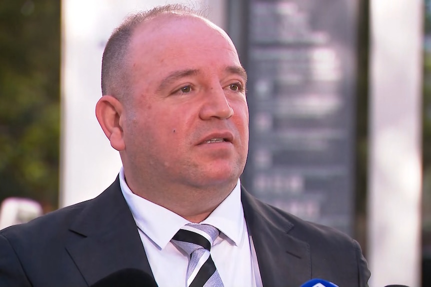 Mr Al Ahmed up close, speaking into a microphone, outside a court, wearing a suit.