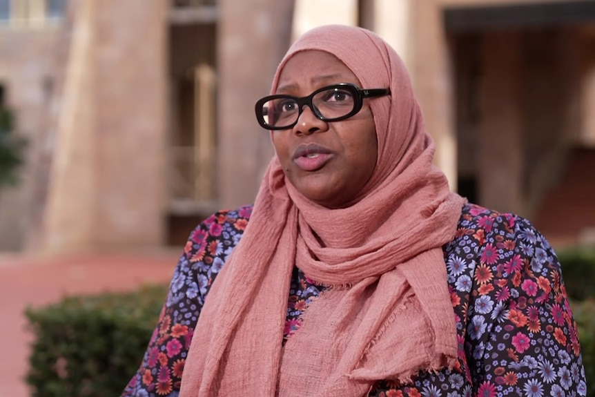 Woman in pink headscarf and black glasses talks