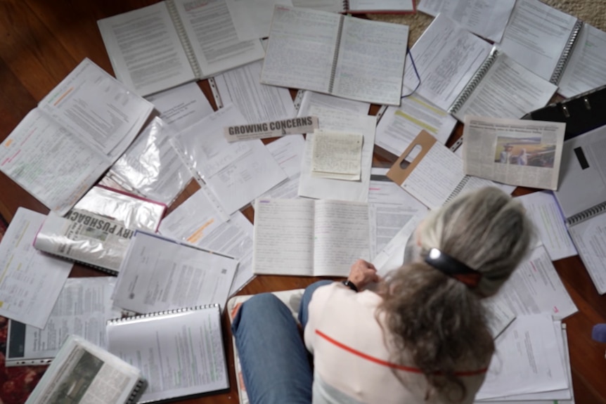 A woman photographed from above, sitting in a home with documents spread out before her.