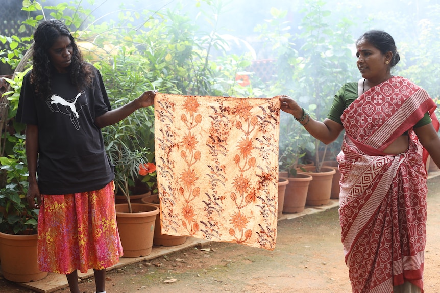 Two women holding up a piece of fabric, which has been decorated with a floral pattern.