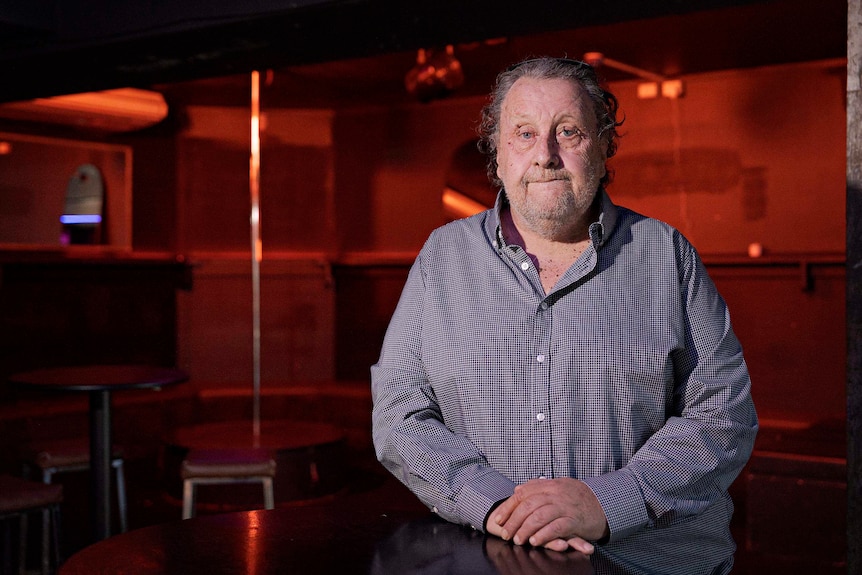A man standing in a darkly-lit nightclub-type room.