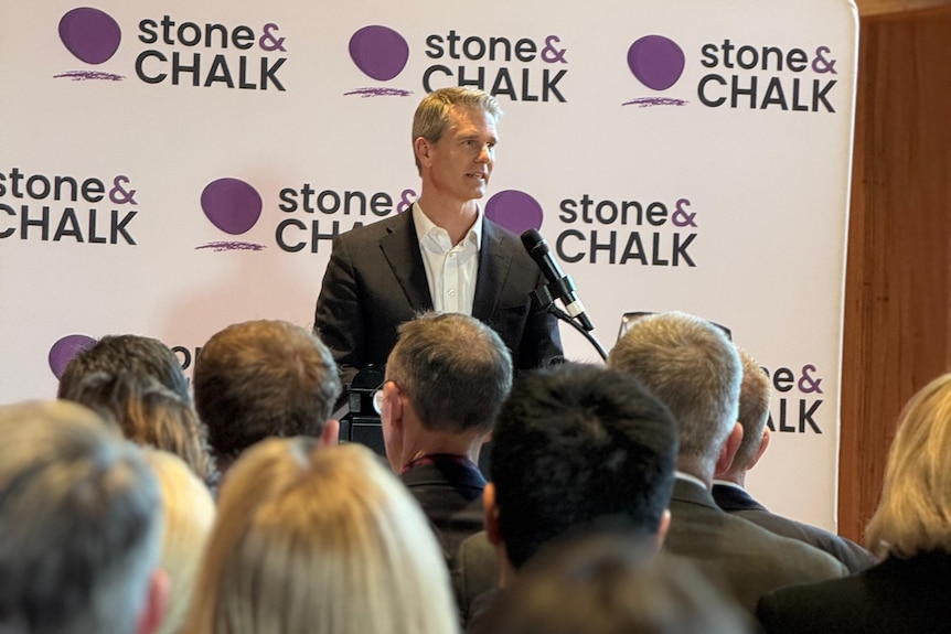A man in a suit speaks in front of a large crowd.