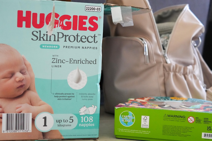 A box of nappies, a box filled with puzzles and a backpack filled with children's clothes rest on the floor.