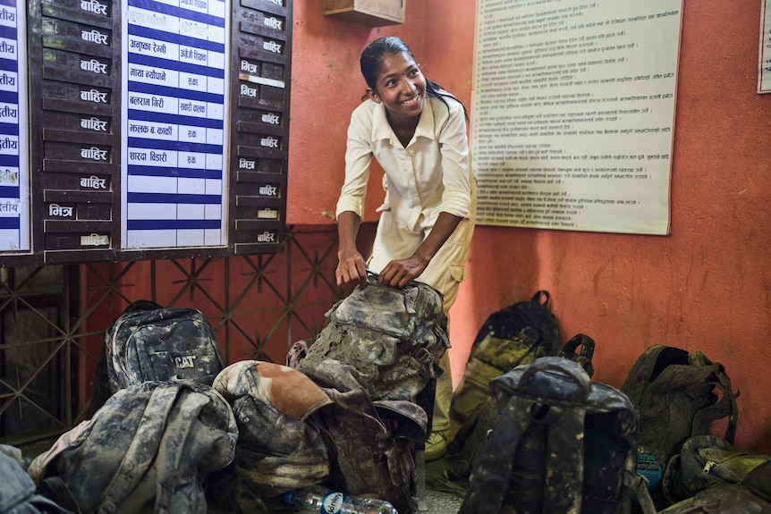 a woman smiles lifting a muddy school bag