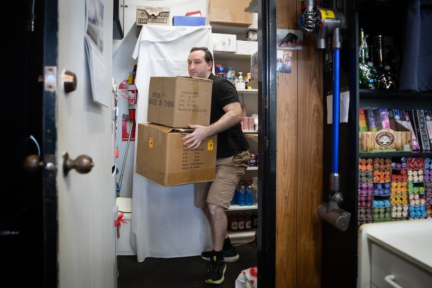 A man carrying boxes inside his tobacco shop.