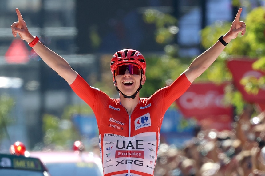 Tadej Pogačar holds up his hands in celebration on the bike