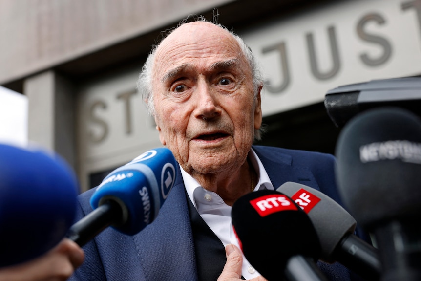 Sepp Blatter with microphones in front of him.