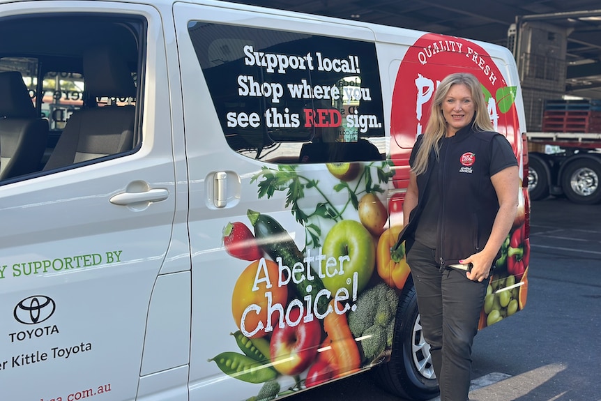 A woman with blond hair stands in front of a white food truck.