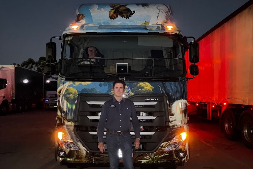 man stands in front of large truck painted in a wildlife them taken in darkness with lights on